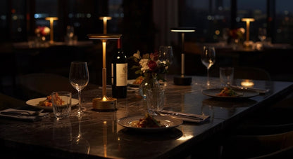 AuraElara Cordless Table Lamp in Gold casting a warm, intimate glow over a luxury dining table setting at night. VelunaLumin.