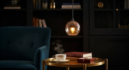 Two LuminaGrace Nordic Wood & Cognac Glass Tall Cylinder Pendant Lights hanging above a modern wooden dining table, casting a warm amber glow, creating an inviting atmosphere, VelunaLumin.