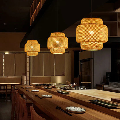 Three ZenWeave 'Tiered Serenity' bamboo pendants hanging over a modern sushi bar, casting a warm, inviting light and creating an authentic, serene oriental atmosphere. VelunaLumin.