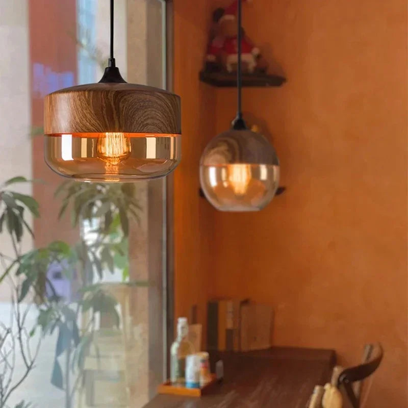 Two LuminaGrace Nordic Wood & Cognac Glass Tall Cylinder Pendant Lights hanging above a modern wooden dining table, casting a warm amber glow, creating an inviting atmosphere, VelunaLumin.
