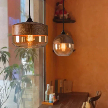 Two LuminaGrace Nordic Wood & Cognac Glass Tall Cylinder Pendant Lights hanging above a modern wooden dining table, casting a warm amber glow, creating an inviting atmosphere, VelunaLumin.